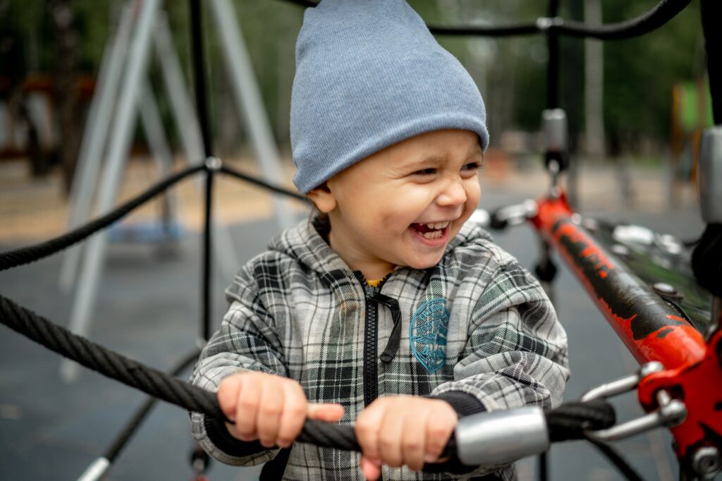 A kid in a gray plaid jacket is playing on a children's playground. The concept of a happy childhood