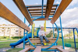 Little girl sits on a wooden bench with rings on the playground